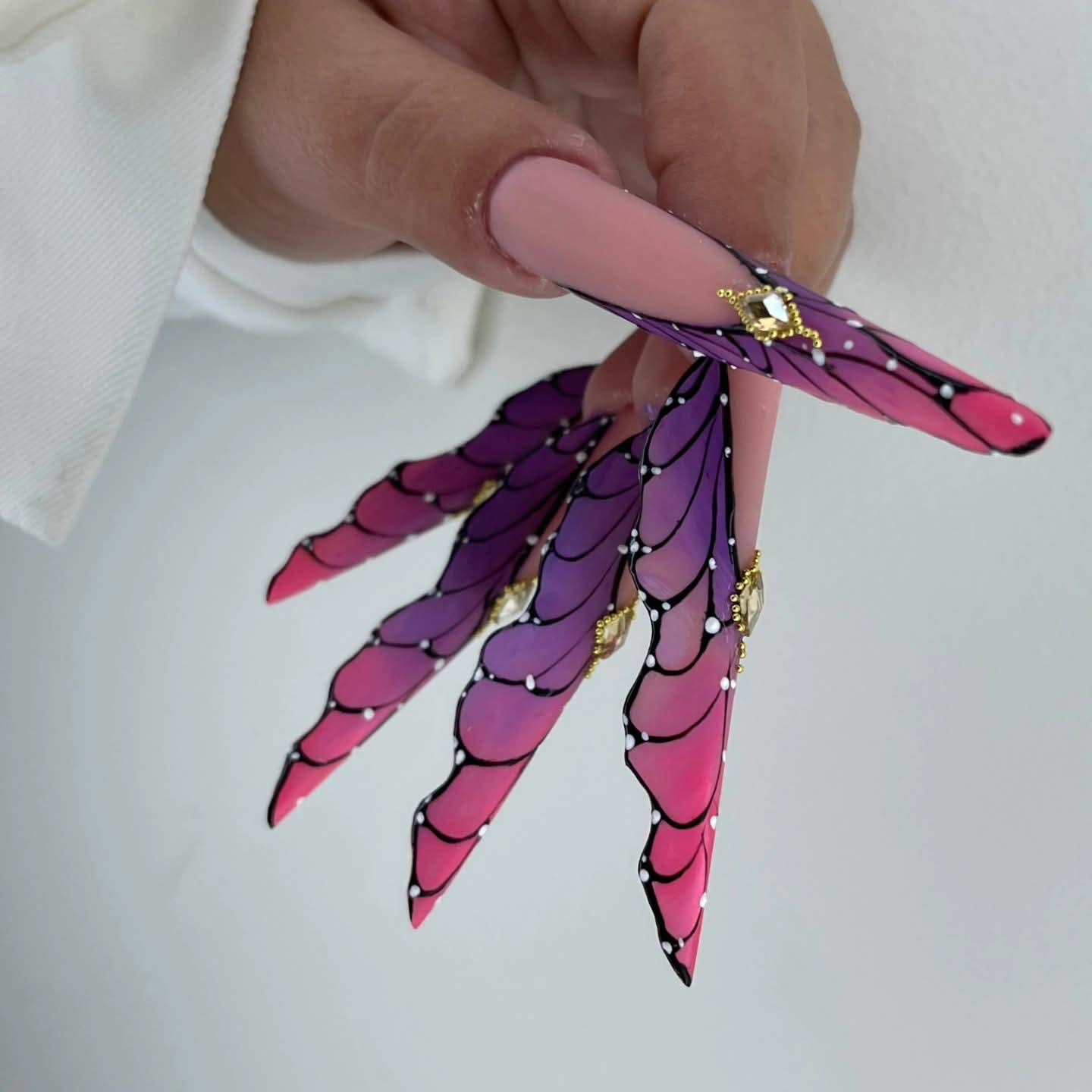 Nail art cu aripi de fluture în nuanțe de roz și mov, cu pietre aurii